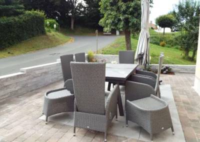 Moderne Terrasse einer Ferienunterkunft in Bolsdorf (bei Hillesheim) mit grauen Rattanmöbeln, großem Esstisch und Sonnenschirm im Grünen.